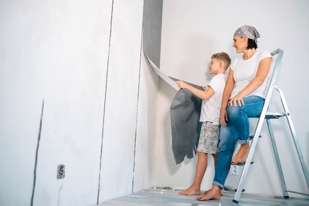 Mother and son take off wallpapers from wall and prepare room for renovationの写真素材