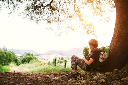 Little backpacker traveler rest under tree on country roadの写真素材