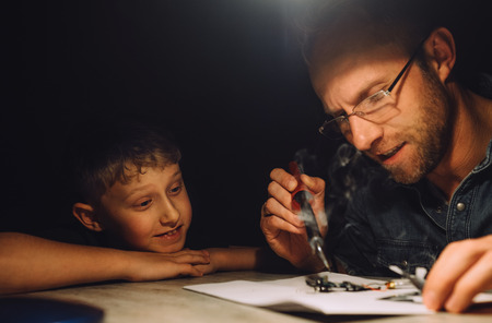 Father soldering with electric soldering iron and his little son watches how he worksの写真素材