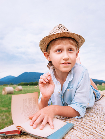 Boy lies on hay roll among the mountain field and reads a bookの写真素材