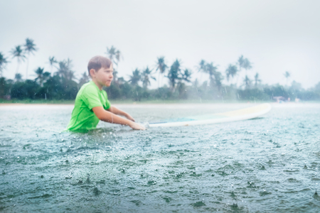 Boy first step surfer learning to surf under the rainの写真素材