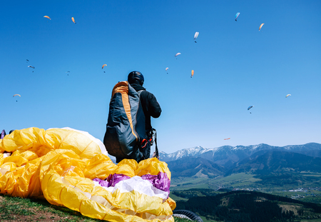 Paraplanner in full equipment for flight looks on soaring another paraplanes in skyの写真素材