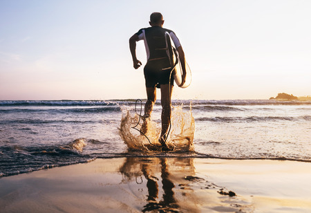 Surfer with surfboard runs in to the ocean wavesの写真素材