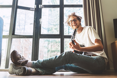 Yong man plays on guitar sitting on the floor in living roomの写真素材
