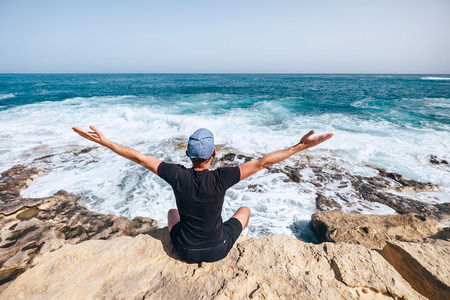 Man sits on rocky cliff near the seaside and looks on wavesの写真素材