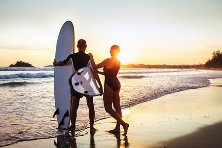 Couple surfers stay on sunset ocean beach