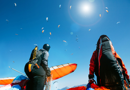 Two paragliders with full flight equipment look on soaring another paragliders in skyの写真素材