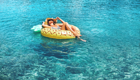 Woman swims on inflatable pineapple ring in the clear sea water. Summer sea vacation