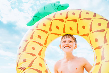 Happy smiling boy portrait with big inflatable pineapple ringの写真素材