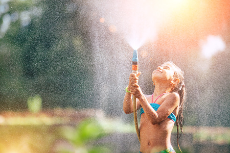 Cute little girl pours herself from the hose, makes a rain. Hot summer day pleasureの写真素材