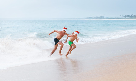 Father and son have a fun on ocean beach, run away from big waves. Christmas holiday time. Tropical vacationの写真素材