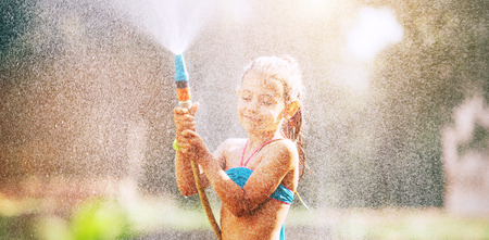 Cute little girl sprinkls a water for herself from the hose, makes a rain. pleasure for hot summer daysの写真素材