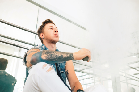 Portrait of modern tattooed art dancer teenager dressed in jeans vest smokes an Electronic cigarette in mirror dance hallの写真素材