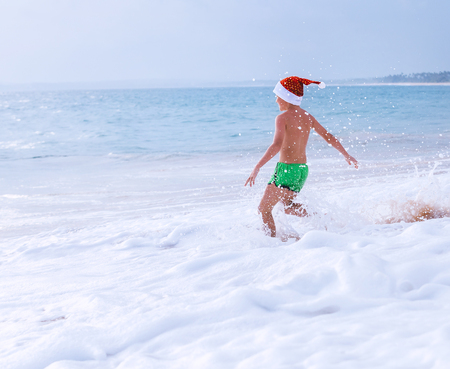 Boy in Santa hat runs to swim in ocean. Christams holiday  time. Tropical vacationの写真素材
