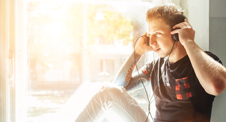 Teenager listening the music sitting on windowsillの写真素材