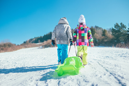Little boy and girl carry the sled and enjoying winter sledding timeの写真素材