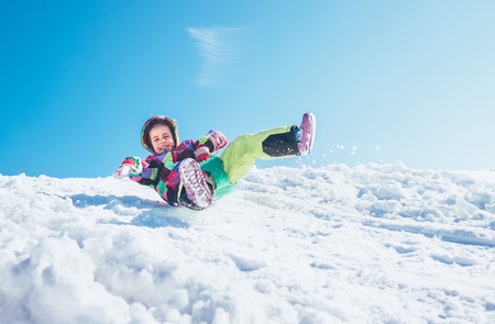 Happy little girl slides down from the snow slopeの写真素材