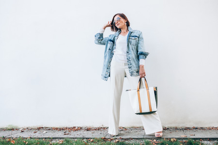 Woman posing in elegant outfit with oversize denim jacket and shopper bagの写真素材
