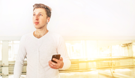 Modern art dancer dressed in white clothes listening a music with smartphone using a headphones in mirror hallの写真素材