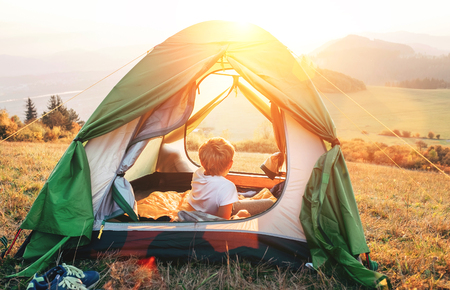 Boy rest in camping tent and enjoy with sunset light in mountain valleyの写真素材