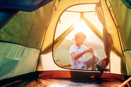 Boy sets up touristic tent ob sunset forest gladeの写真素材
