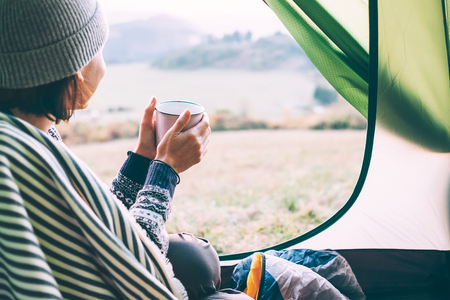 Woman with cup of hot tea sit in camping tentの写真素材