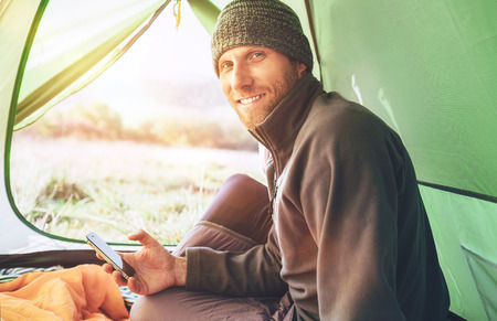 Bearded traveler Man uses his mobile phone sitting in tentの写真素材