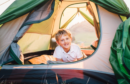 Happy smiling boy rest in tent at sunset time in mountainの写真素材
