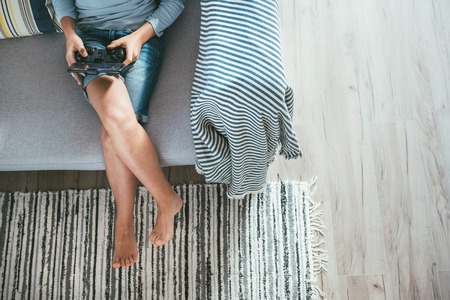 Boy sits on sofa plays with smartphone and gamepad camera top view.の写真素材