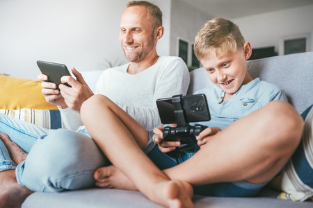 Father and son, PC gamers, enthusiastically playing with electronic devices: tablet and gamepadの写真素材