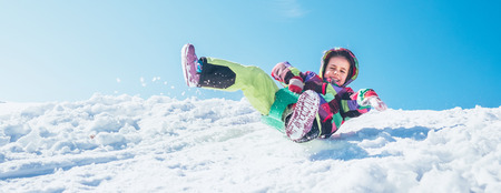 Little Happy girl slides down from the snow slope with blue skyの写真素材