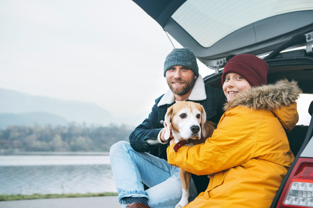 Father and son with beagle dog siting together in car trunk and smiling into camera.の写真素材