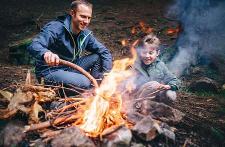 Father and son make bonfire in forest. Camping trip at spring or autumn timeの写真素材
