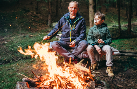 Father and son roast marshmallow candies on campfire in forestの写真素材