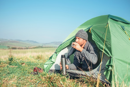 Man traveler meets new day in tent, drinks hot tea sitting insideの写真素材