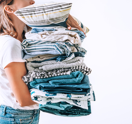 Woman takes in hands big pile blue and beige blankets, towels and other home textileの写真素材