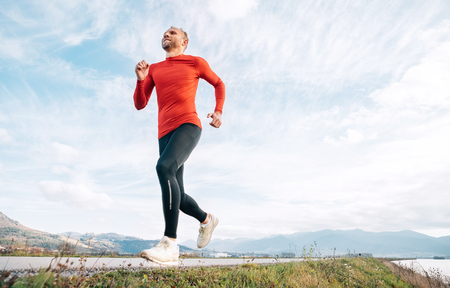 The wide angle shoot of a Man dressed in red long sleeve shirt runs by the road with mountainの写真素材