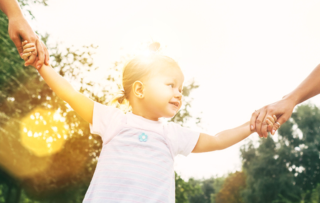 Little girl holds parents hands during the sunny day city park walkingの写真素材