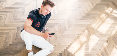 Young man using his smartphone with headphones, listen the music and sit on the floorの写真素材