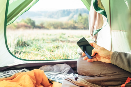 Traveler uses mobile phone sitting in tent. Close up image man hands with mobile phoneの写真素材