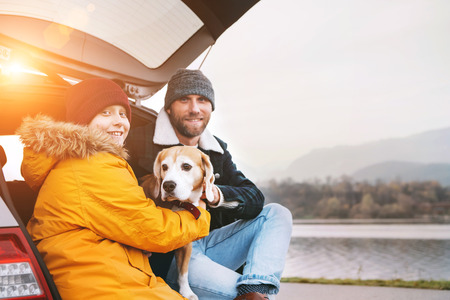 Father and son with beagle dog siting together in car trunk and smiling into camera.の写真素材