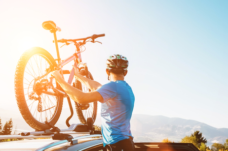 Mountain biker man take of his bike from the car roof evening sunset imageの写真素材