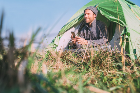 Traveler catch cellular network and use his mobile phone sitting in tent.の写真素材
