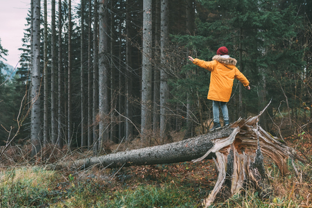 Boy in bright yellow parka (puffer jacket) walks in pine forest on the falling treeの写真素材