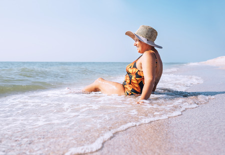 Senior woman enjoy beach vacation sitting on the sea surflineの写真素材