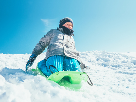 Happy boy slides down from snow hill using the sledge. Winter outdoor activityの写真素材
