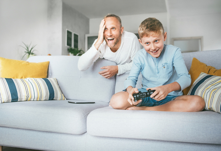 Father watching his son playing TV video game using the game pad and emotional reacts.の写真素材