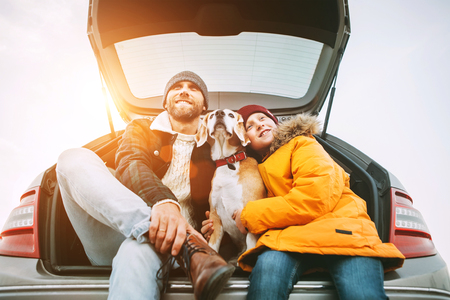 Father and son dressed in yellow warm jacket with beagle dog siting together in car trunk.の写真素材