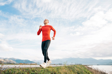 Wide angle shoot of a Man dressed in red long sleeve shirt runs by the road with mountainの写真素材