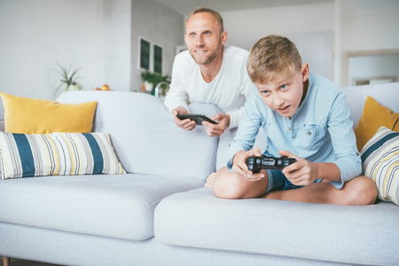 Father watching his son playing TV video game using the game pad in the living room.の写真素材